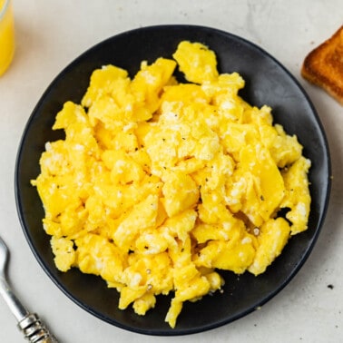 Overhead view of scrambled eggs on a black plate with toast on the side.