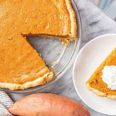 Bird's eye view of full Sweet Potato Pie with a single slice cut out and placed on a white plate topped with whipped cream.