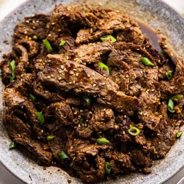 Plate of cooked bulgogi meat surrounded by ingredients.