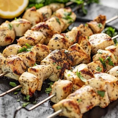 Lemon Chicken Kabobs garnished with lemon halves and parsley on a black plate.