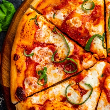 Overhead view of margherita pizza with a side small bowl filled with marinara dipping sauce.