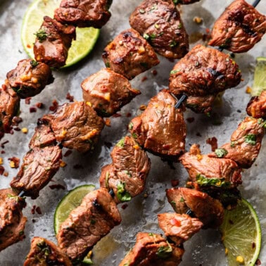 Four marinated beef kebabs are laid out on a tray.