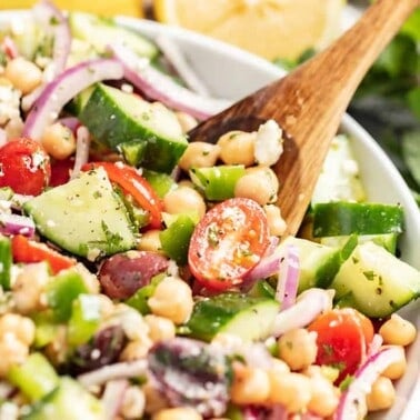 A bowl of mediterranean chickpea salad with a wooden spoon.