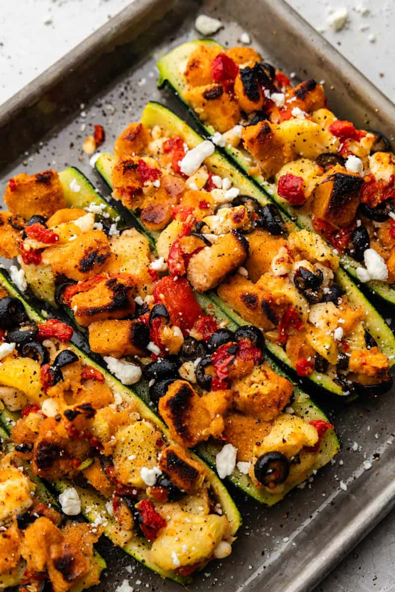 An overhead view of zucchini boats stuffed with olives, croutons, roasted red bell peppers, and feta.