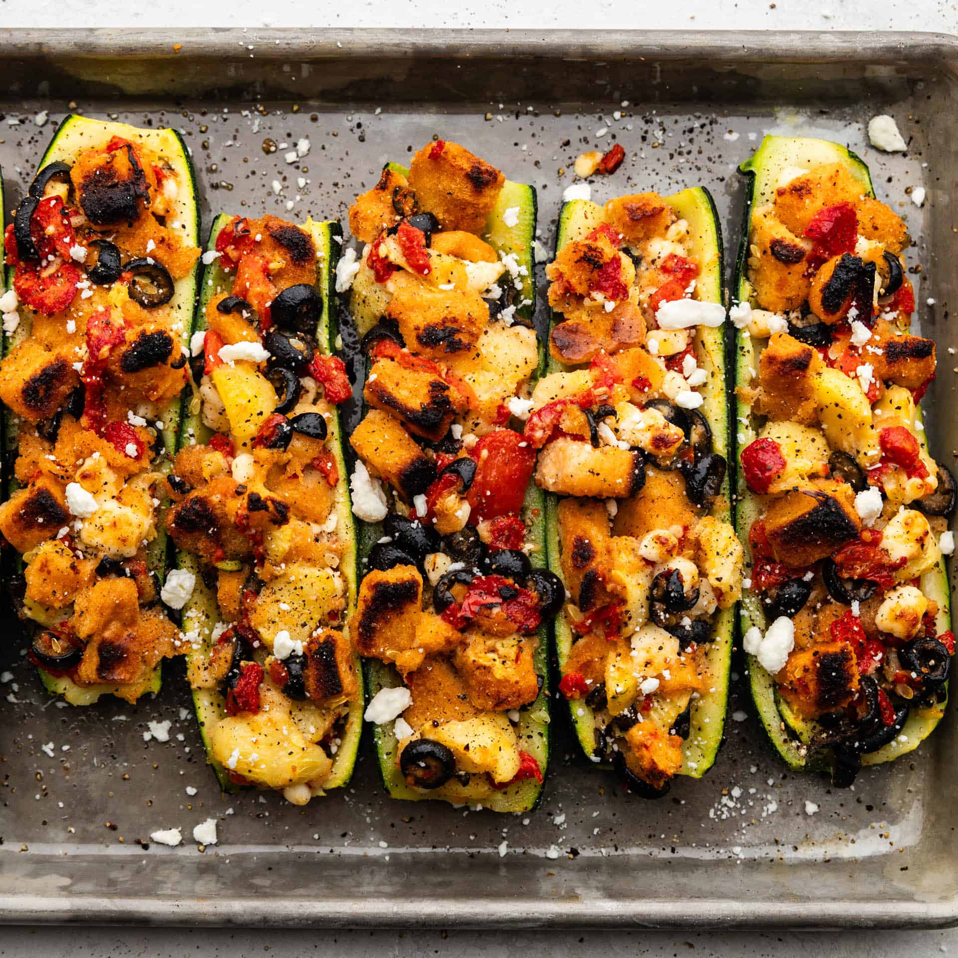 An overhead view of mediterranean stuffed zucchini boats on a baking sheet.