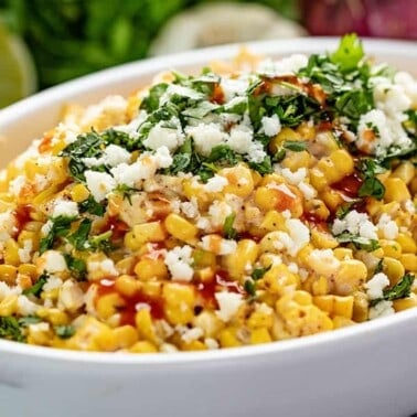 Angled view of Mexican Street Corn Salad in a white dish drizzled with hot sauce.