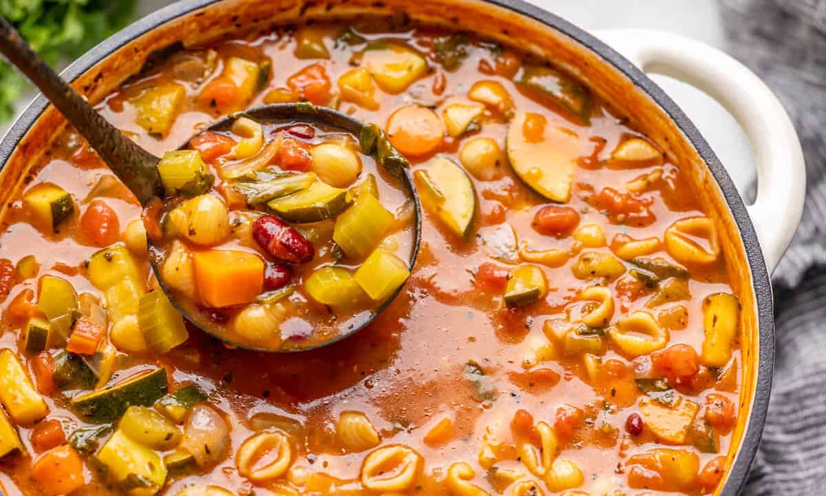 A ladle full of minestrone soup being scooped out of a soup pot.