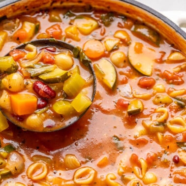 A ladle full of minestrone soup being scooped out of a soup pot.