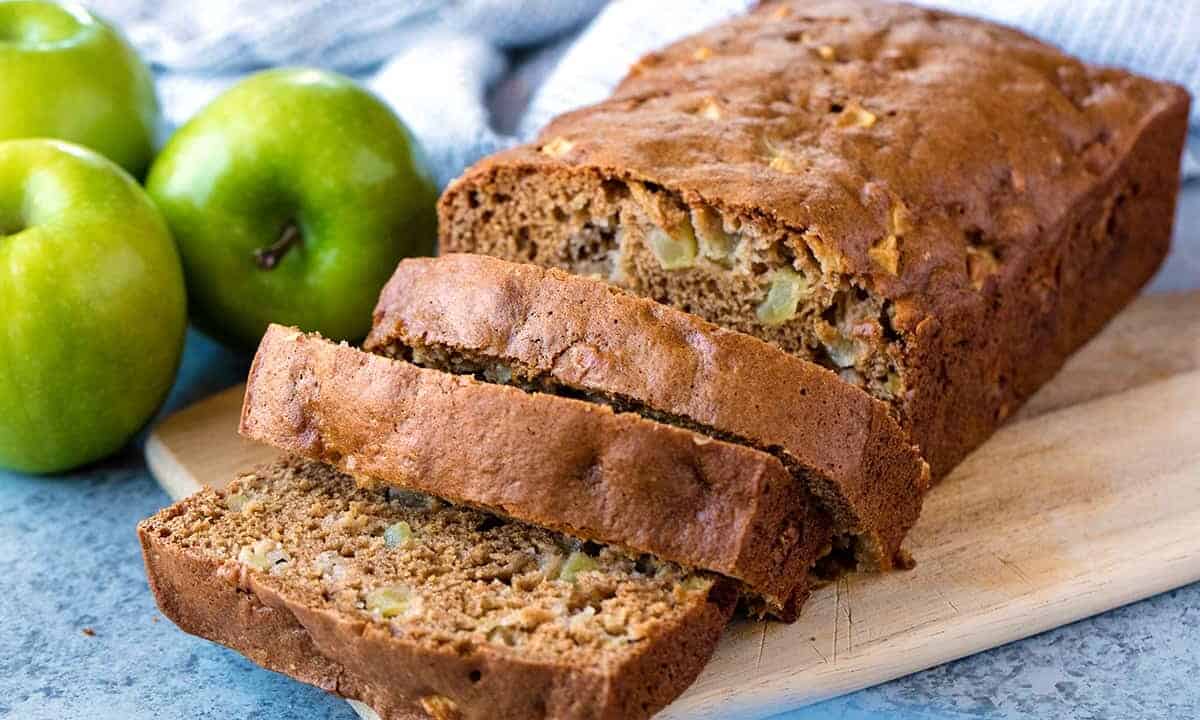 Sliced loaf of moist cinnamon apple bread on a cutting board.