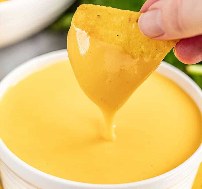 A hand dipping a tortilla chip into a small bowl of cheese sauce