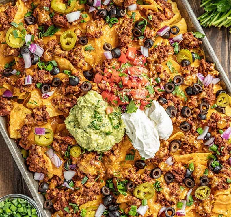 Nachos on a baking sheet with salsa and green onions on the side