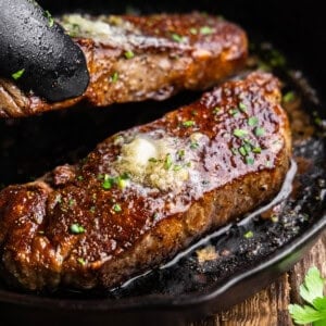 A close up view of two new york strip steaks in a skillet with resting butter on top.