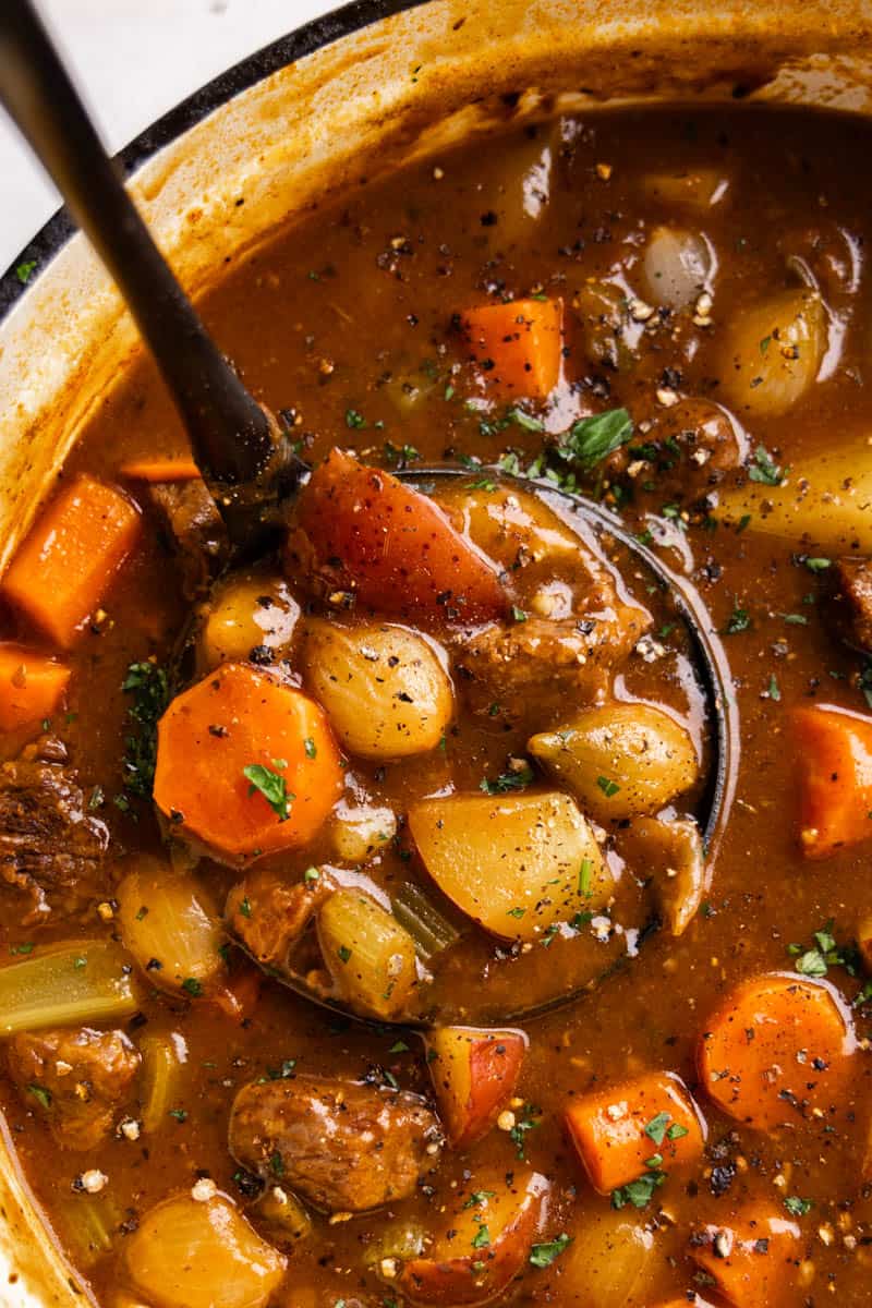 A close up view of a ladle of beef stew being scooped out of the pot. 