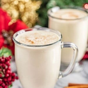 Two glass mugs filled with homemade eggnog and surrounded by holiday decorations.