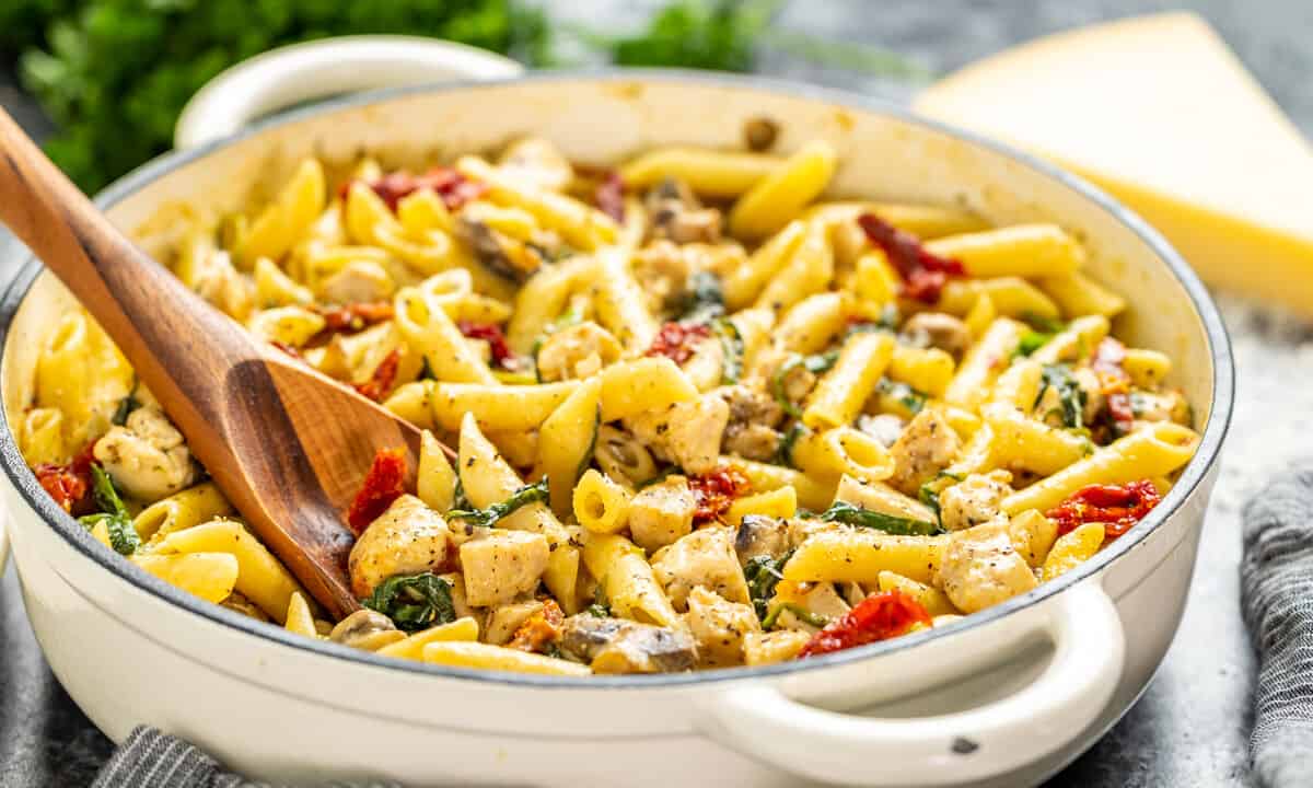 A wooden spoon resting in a pot of Italian chicken and pasta.