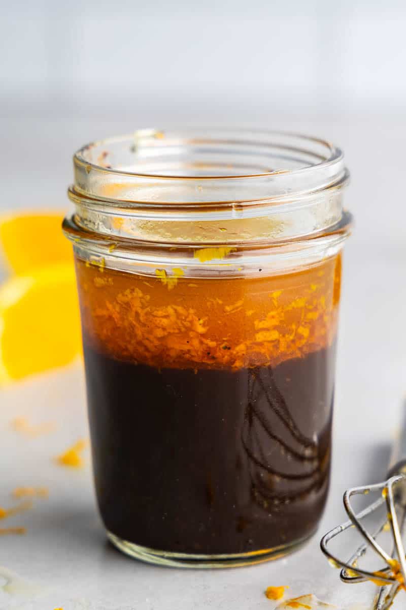 A close up view of a jar of orange balsamic vinaigrette salad dressing. 