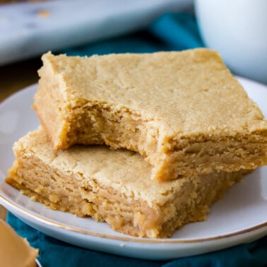 Peanut Butter Blondies stacked on a plate. One with a bite taken out of it