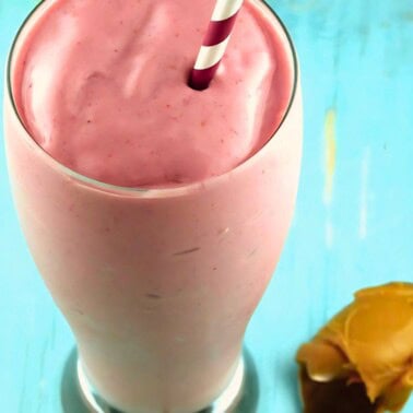 A pink peanut butter and jelly smoothie with a spoon of peanut butter laying next to it.