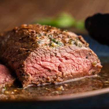 A close up view of a petite tender steak that has already been cut into showing a perfectly pink interior.