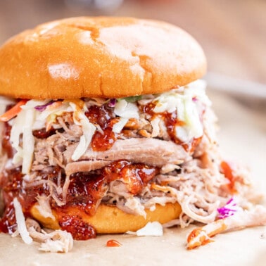 Close up view of a pulled pork sandwich that is overflowing with fillings.