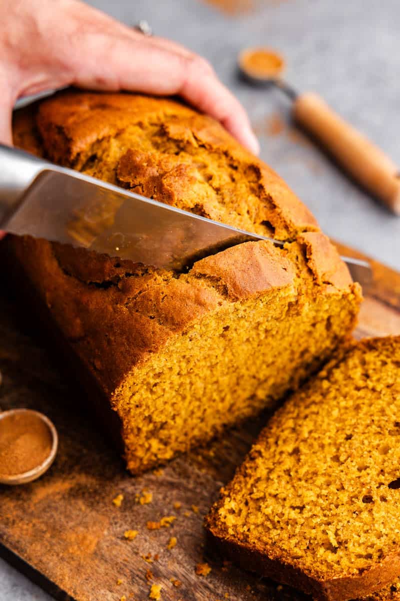 A close up view of a loaf of pumpkin bread being sliced on a cutting board.