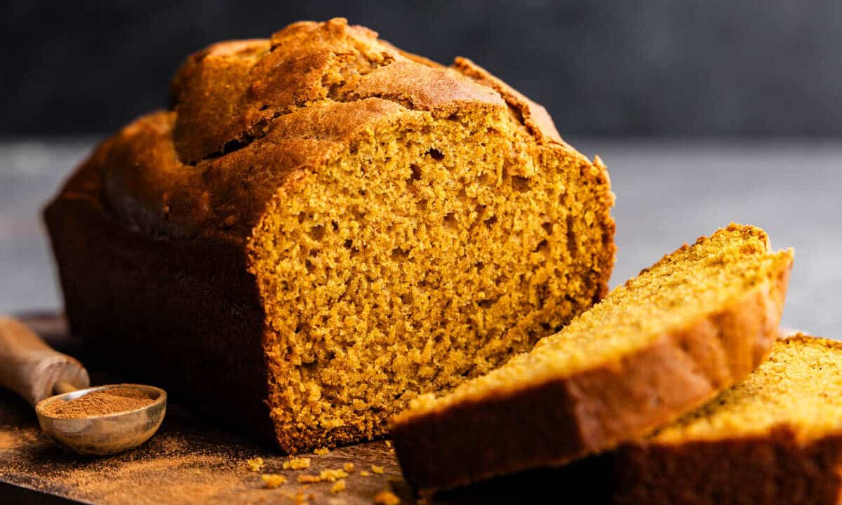 A loaf of pumpkin bread on a cutting board. Two slices have already been cut.