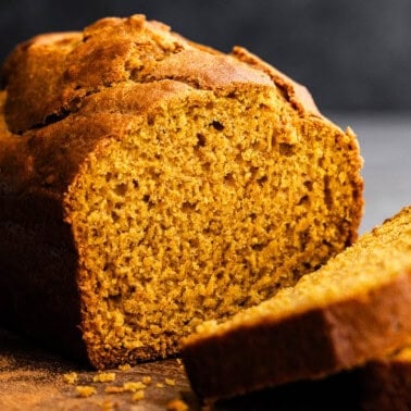 A loaf of pumpkin bread on a cutting board. Two slices have already been cut.