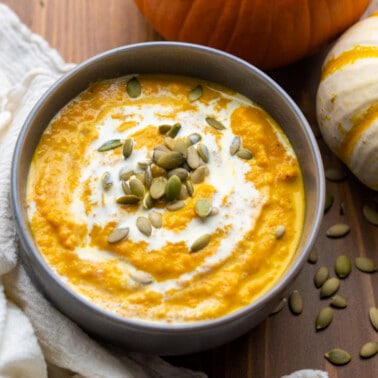 Overhead view looking into a bowl filled with creamy pumpkin soup and pumpkin seeds on top.