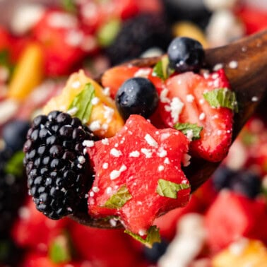 A bowl of red, white, and blue fruit salad with a wooden spoon.