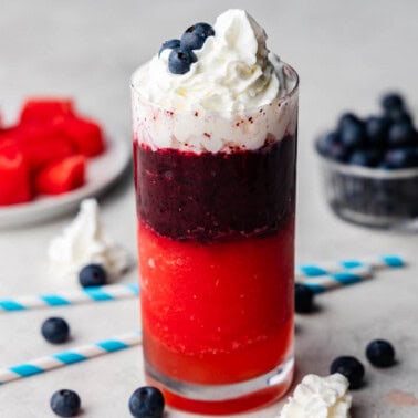 A Red, White, and Blue Slushy with watermelon and blueberries around it.