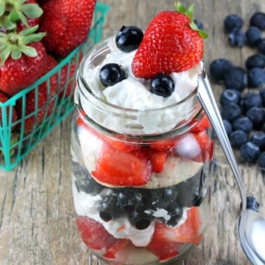 Red, White, and Blueberry Mason Jar Shortcake on a wooden counter.