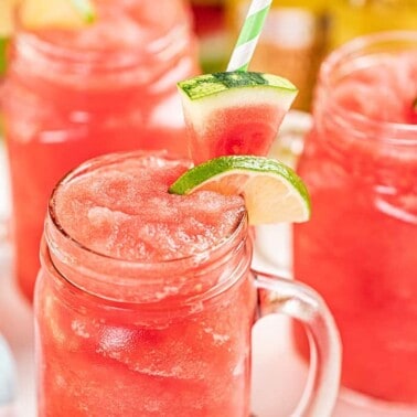 Watermelon slushies in drinking glasses with lime and watermelon wedges on the rim.