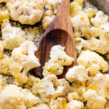 Close up of roasted cauliflower on a pan with a wooden spoon on it.