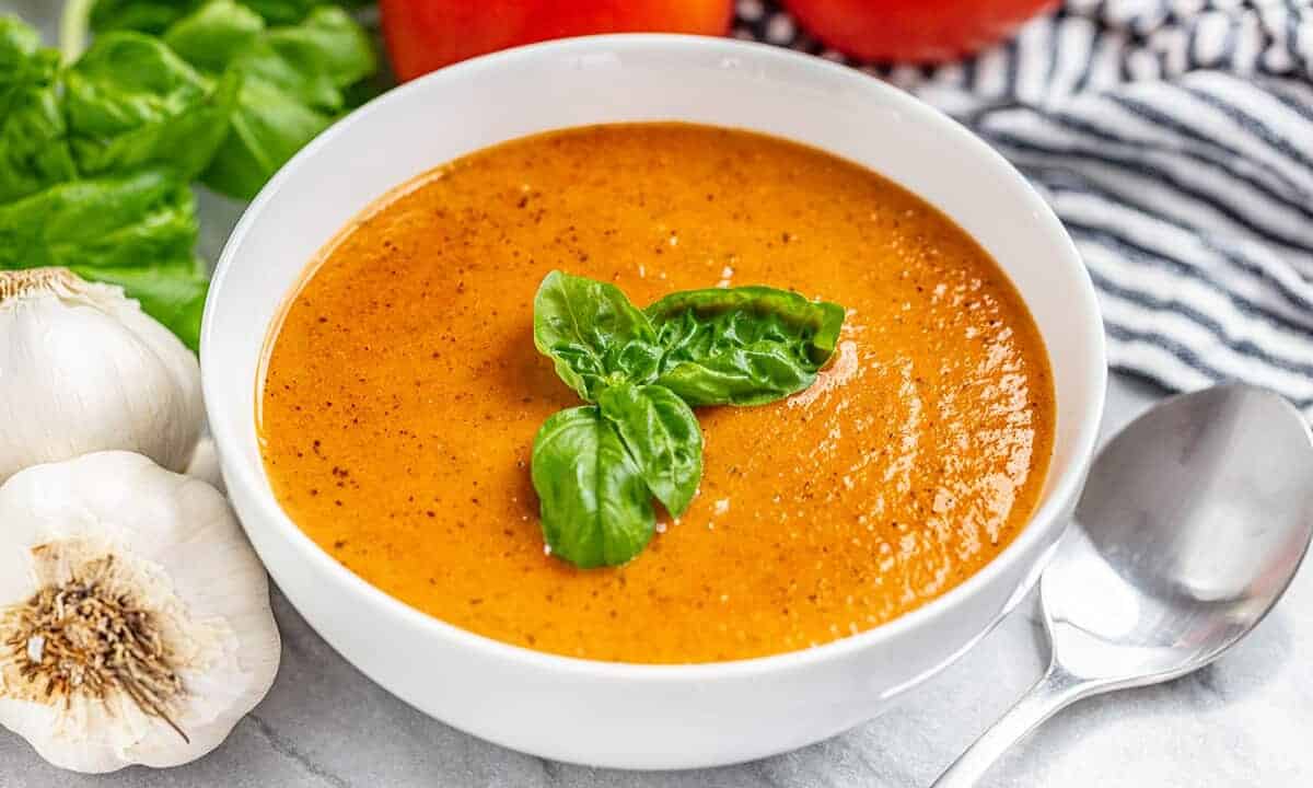 A bowl of tomato basil soup with fresh basil on top and a spoon next to the bowl