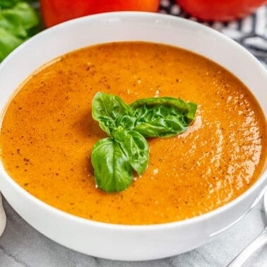 A bowl of tomato basil soup with fresh basil on top and a spoon next to the bowl