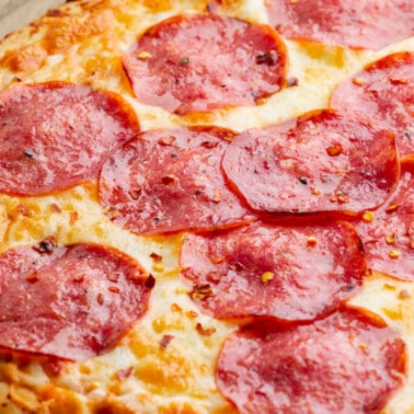 Close up view of a salami pizza on a wood tray.