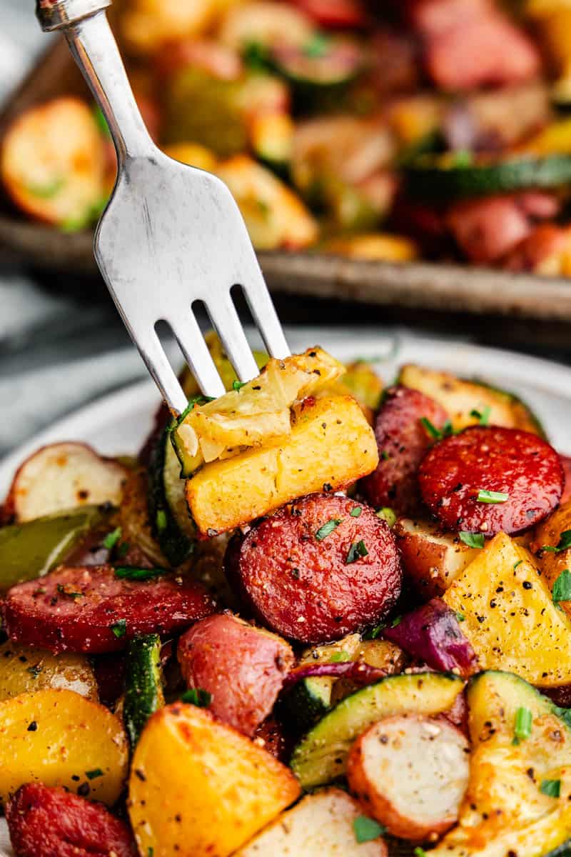 A close up picture of a fork spearing veggies and sausage off a plate.