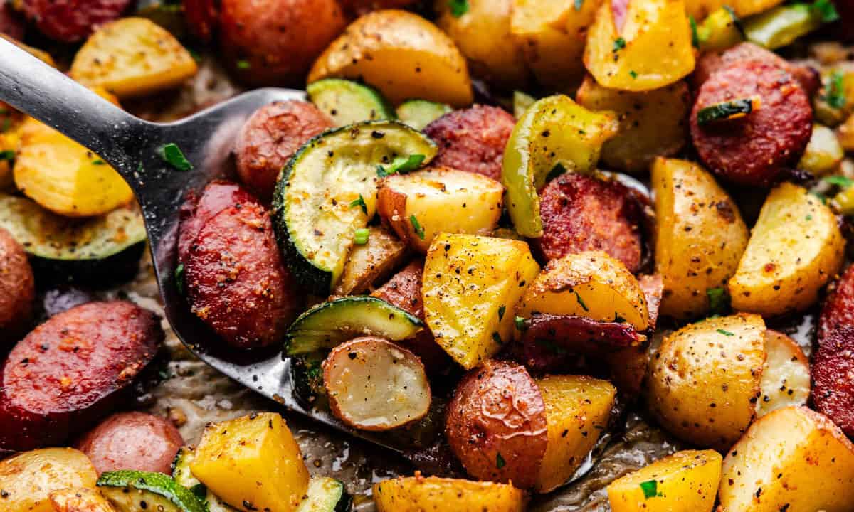 A close up view of a spatula lifting diced potatoes, peppers and sausage coins.