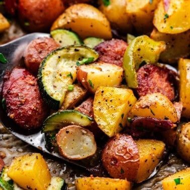 A close up view of a spatula lifting diced potatoes, peppers and sausage coins.