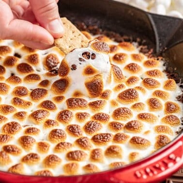 A hand dipping a graham cracker into s'mores dip.