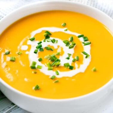 Sweet Potato Soup in a white bowl topped with cream and green onions.