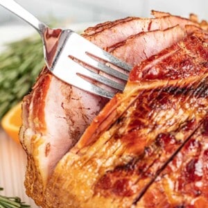 A serving utensil pulling out a piece of orange glazed ham.