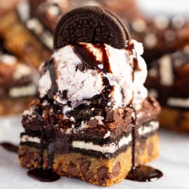 Close up of Slutty Brownies topped with a single scoop of vanilla ice cream and one whole Oreo cookie and drizzled with chocolate syrup.