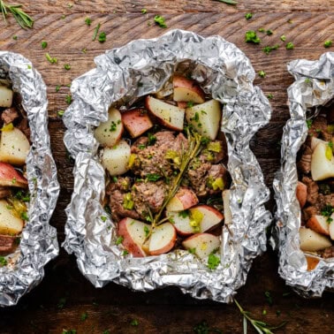 Three foil packets with cooked steak and potatoes.