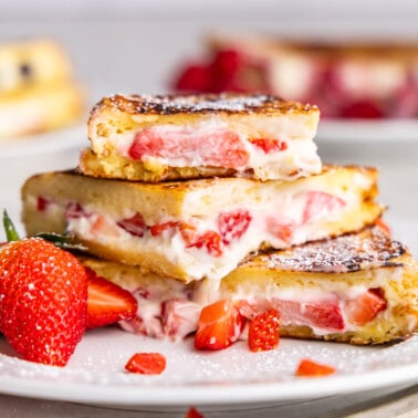 A white plate with French toast stuffed with cream cheese and strawberries.