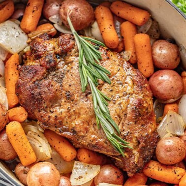 Bird's eye view of Pork Roast garnished with a rosemary sprig, carrots, baby red potatoes, and onion in a cast iron dutch oven.