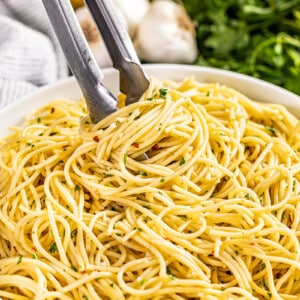 Tongs inside a bowl filled with olive oil pasta.