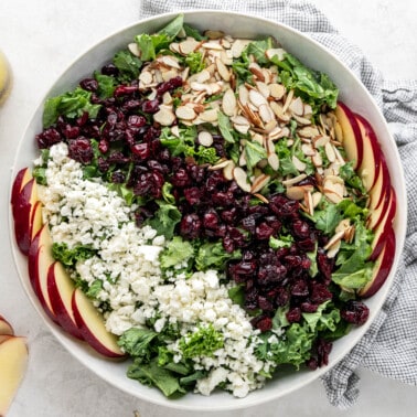 Overhead view of a kale salad in a large serving bowl with the dressing on the side.