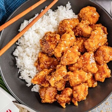 Overhead view of a bowl of white rice with takeout sesame chicken.