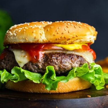 A close up view of a perfect juicy hamburger on a black plate with french fries in the background.